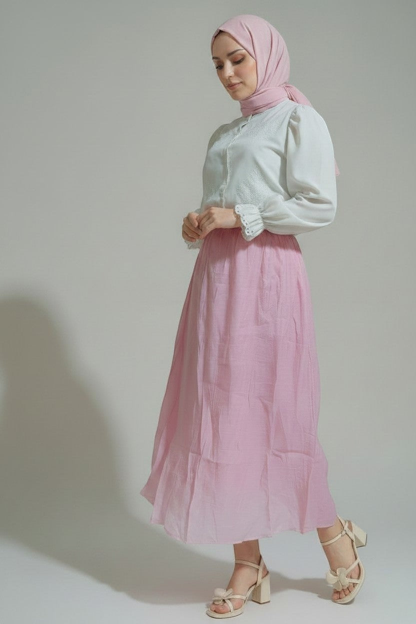 VELLA pembe keten karışımlı, yüksek bel, dökümlü uzun etek. Model, beyaz işlemeli bluz ve topuklu sandalet ile kombinlenmiştir.